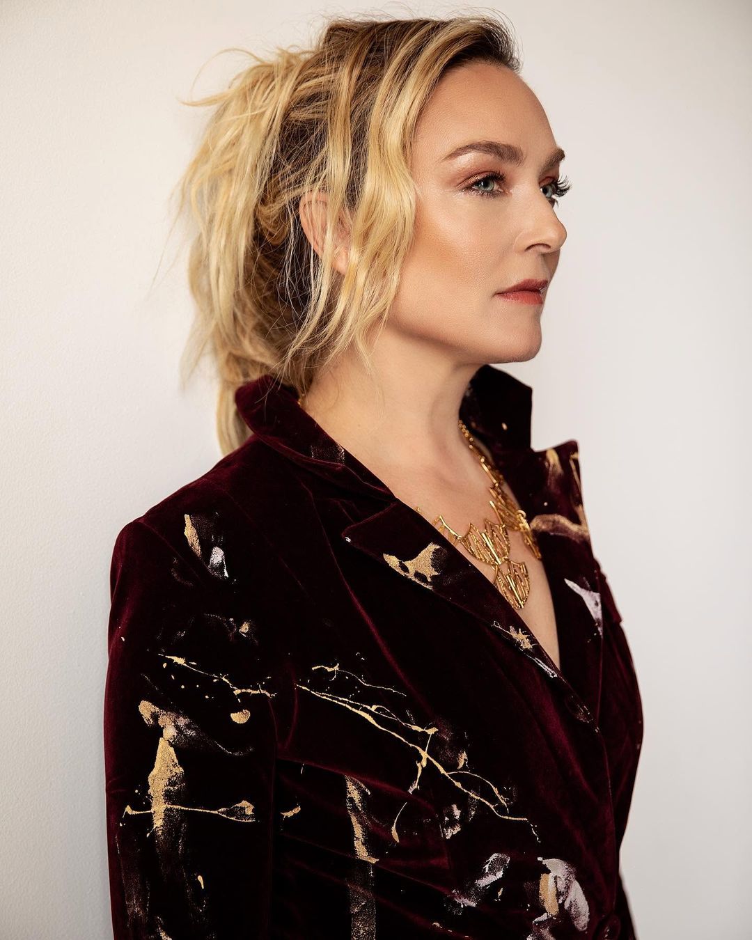 Elisabeth Röhm in profile wearing a paint-splashed burgundy velvet blazer and a gold necklace for Jejune Magazine, styled by Quentin Fears