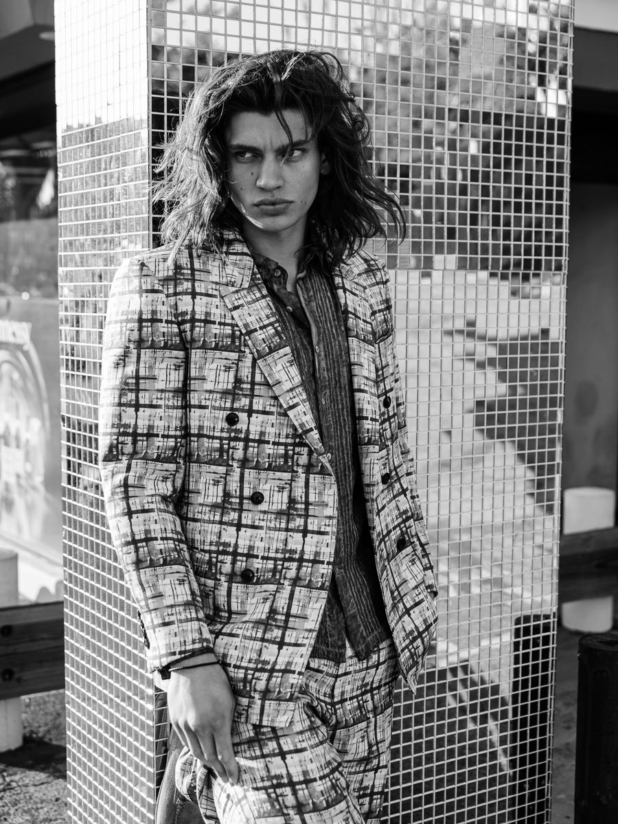 Menswear editorial: an oversized checked coat against a mirrored mosaic wall