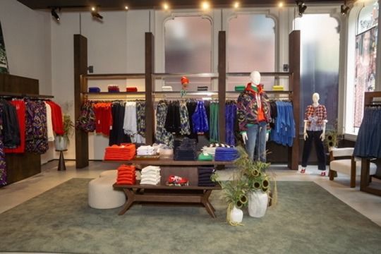 The pop-up's main floor: color-grouped racks, folded knits stacked on a wood table, and styled mannequins