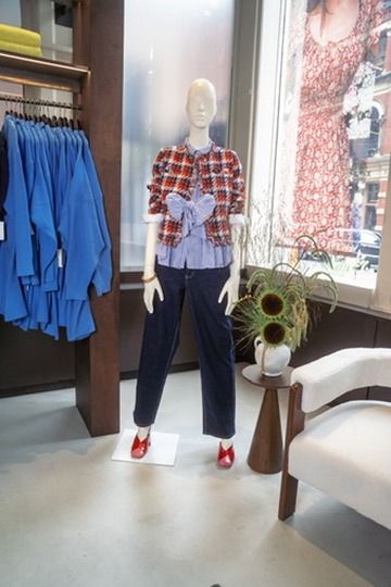 A mannequin in a red plaid jacket over a tied blue shirt, dark jeans and red flats beside the shop window
